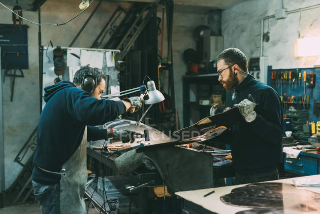 Métallurgistes masculins martelant le cuivre à l'établi de forge — Photo de stock