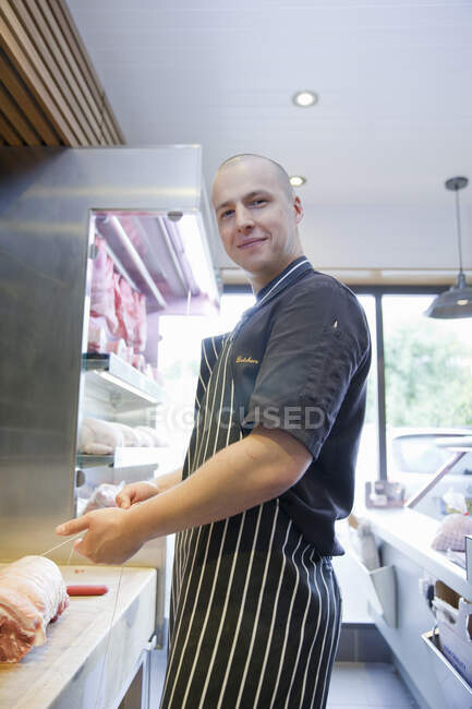 Portrait of butcher tying meat joint in butchers shop — Stock Photo