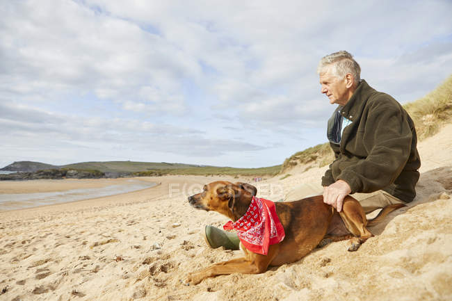 Homem e cão sentados na praia, Constantine Bay, Cornwall, Reino Unido — Fotografia de Stock