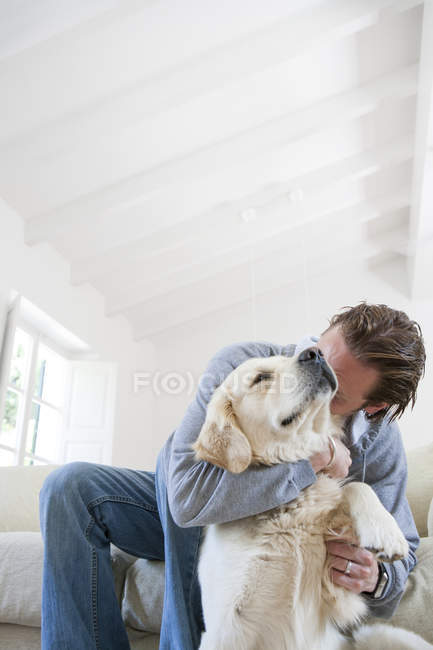 Young man on living room sofa hugging golden retriever dog — Stock Photo