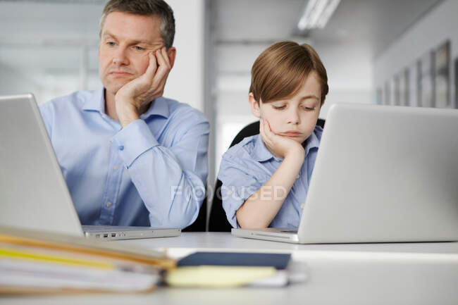 Vater und Sohn schauen gelangweilt mit Laptops — Stockfoto