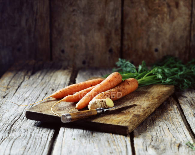 Cenouras e gengibre em tábua de madeira com faca — Fotografia de Stock