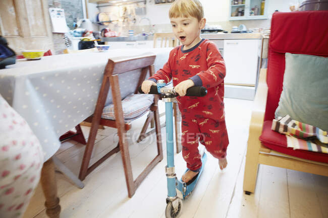 Young boy playing on scooter in kitchen — Stock Photo