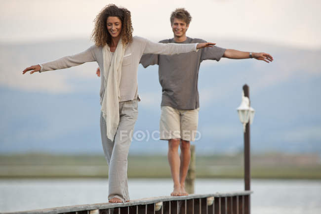 Young couple balancing on wooden jetty by water — Stock Photo