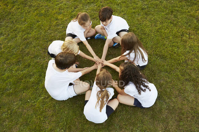Vista aérea de niño y niña deporte equipo sentado en la hierba en círculo en el campo de juego - foto de stock