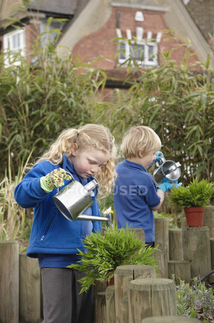School boy and girl watering plants in garden — Stock Photo