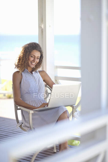 Junge Frau benutzt Laptop auf Balkon eines Strandhauses — Stockfoto