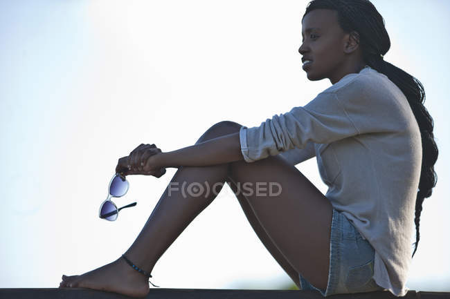 Retrato de jovem sentada, segurando óculos de sol — Fotografia de Stock