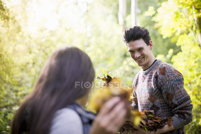 Молода пара грає з осіннім листям у лісі — стокове фото
