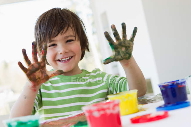 Усміхнений хлопчик малює пальцями в приміщенні — стокове фото