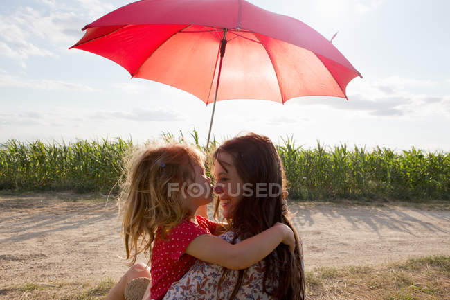 Mother and daughter hugging under red umbrella — Stock Photo
