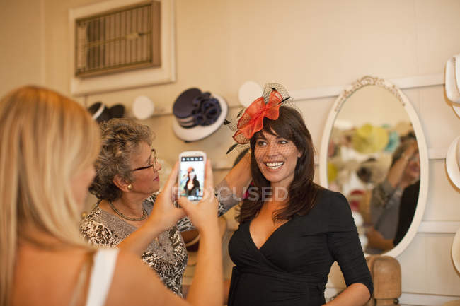 Women taking picture in fancy hat in traditional milliner shop — Stock Photo