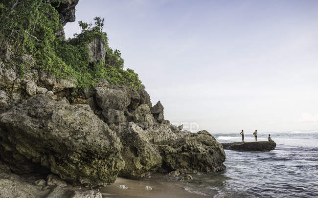 Tres hombres en la roca costera en Panawa Beach, Bali, Indonesia - foto de stock