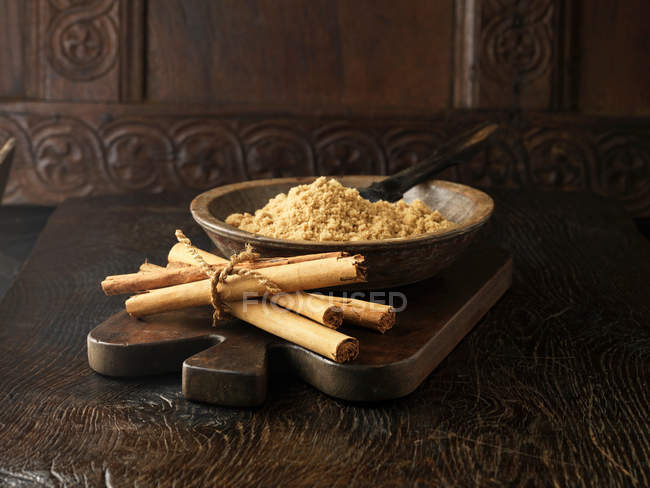 Paus de canela amarrados com fio e açúcar mascavo em tigela de madeira — Fotografia de Stock