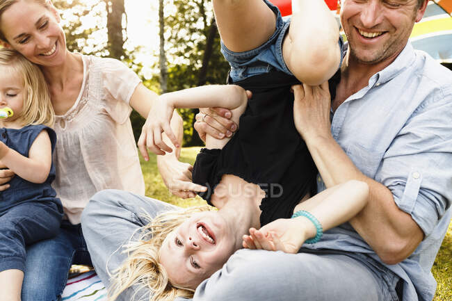 Padre poniendo a su hija patas arriba en el picnic familiar en el parque - foto de stock