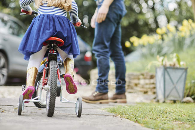 Отец учит дочь ездить на велосипеде по улице — стоковое фото