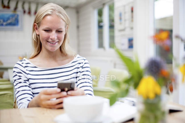 Молода жінка в кафе дивиться на мобільний телефон — стокове фото