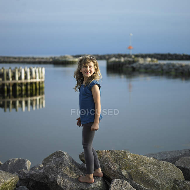 Chica de pie en la roca por el lago - foto de stock