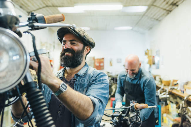 Двое зрелых мужчин работают на мотоцикле в гараже — стоковое фото