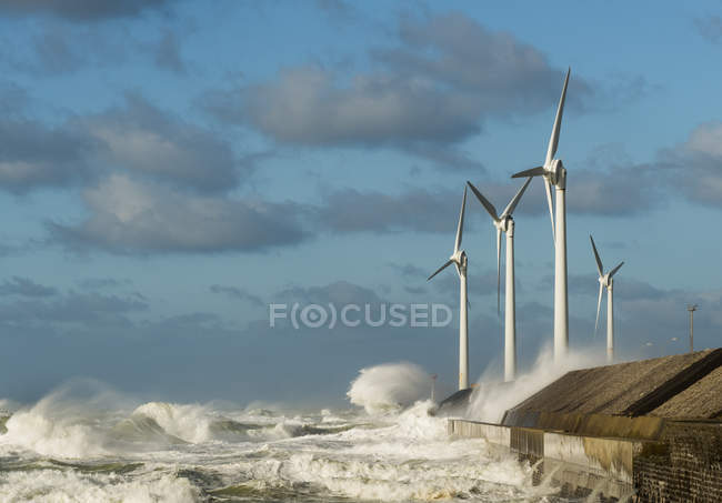 Turbinas eólicas con olas de tormenta y nubes en la costa - foto de stock