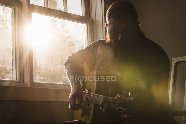 Homem tocando guitarra ao lado da janela — Fotografia de Stock