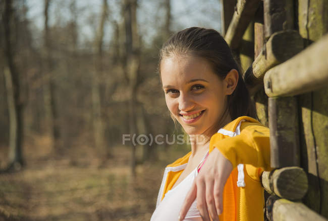 Portrait of young woman leaning against fence in forest — Stock Photo