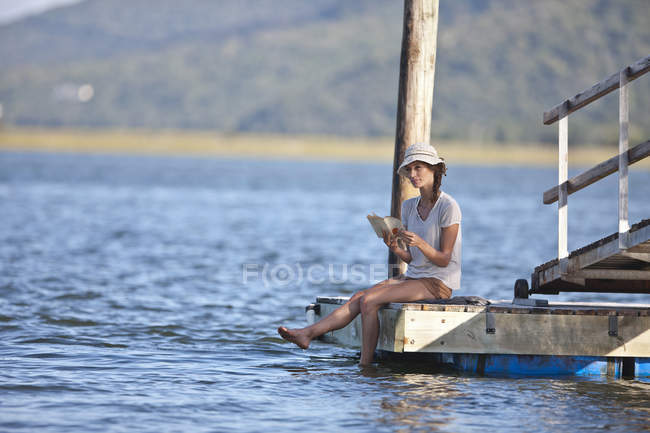 Молодая женщина, сидящая на причале и читающая книгу — стоковое фото