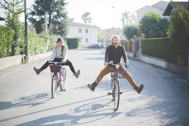Jovem casal de bicicleta com as pernas para fora — Fotografia de Stock