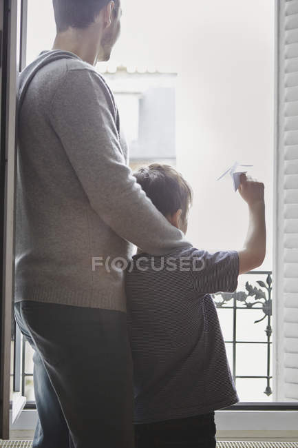 Niño lanzando avión de papel con padre desde la ventana - foto de stock