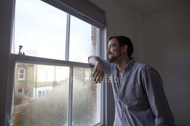 Mid adult man looking out through bedroom window — Stock Photo