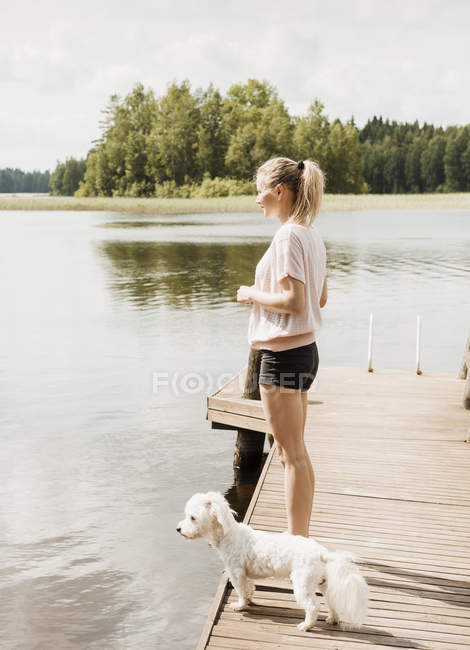 Жінка, стоячи з Котон де тулеар собакою на озері пристані, Orivesi, Фінляндія — стокове фото