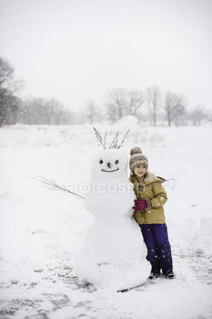Ragazza che spala neve davanti al pupazzo di neve, Lakefield, Ontario, Canada — Foto stock