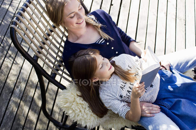 Мать и дочь отдыхают на шезлонге, девочка читает книгу — стоковое фото