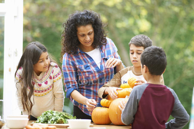 Mature mother and three children selecting homegrown pumpkins in kitchen — Stock Photo