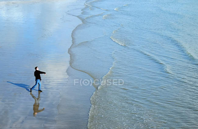High angle side view of mature man on beach throwing stones into ocean — Stock Photo