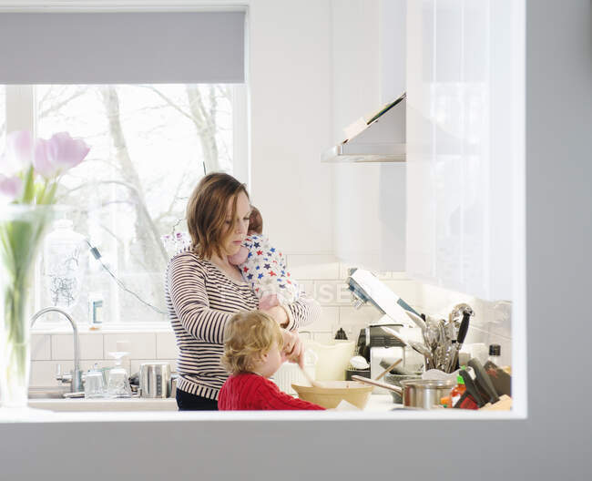 Mother with baby and toddler in kitchen — Stock Photo