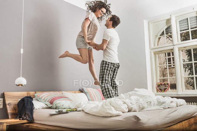 Couple wearing pyjamas jumping on bed — Stock Photo