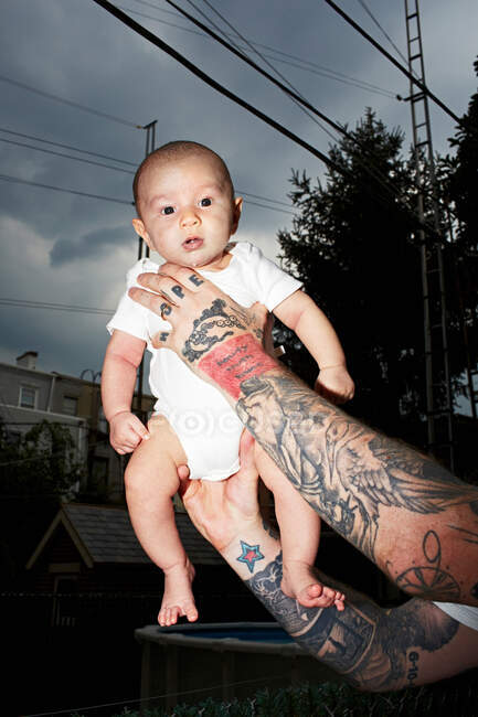Padre con le braccia tatuate che tiene in braccio il bambino — Foto stock