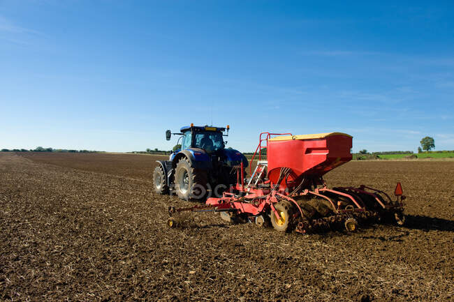 Rear view of farmer driving tractor with seed drill in ploughed field in spring — Stock Photo