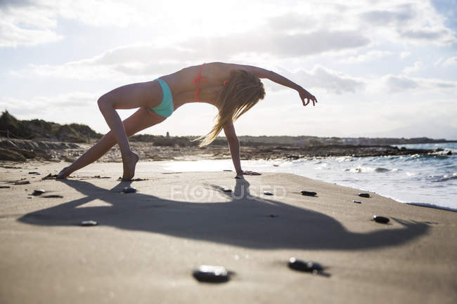 Young woman on beach, in yoga position, rear view — Stock Photo