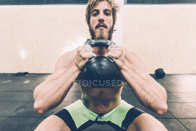 Portrait of young male cross trainer training with kettlebell in gym — Stock Photo