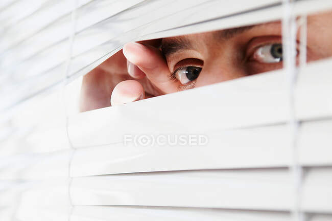 Hombre mirando a través de las persianas de oficina - foto de stock