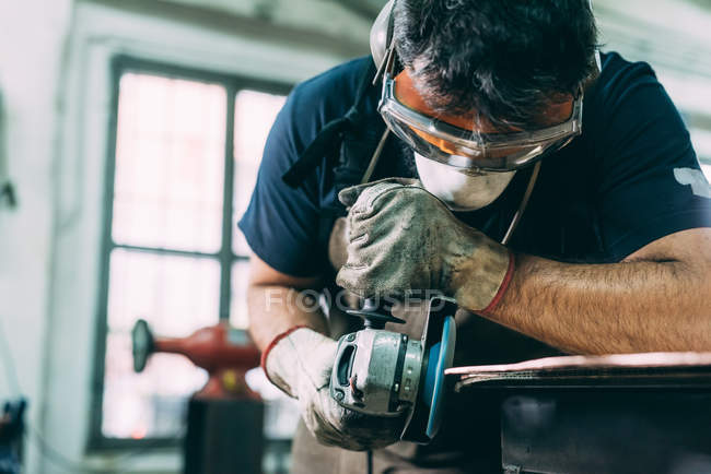 Metalworker grinding the edge of copper in forge workshop — Stock Photo