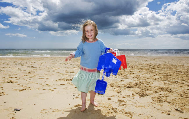 Chica joven sosteniendo cubo y pala en la playa - foto de stock