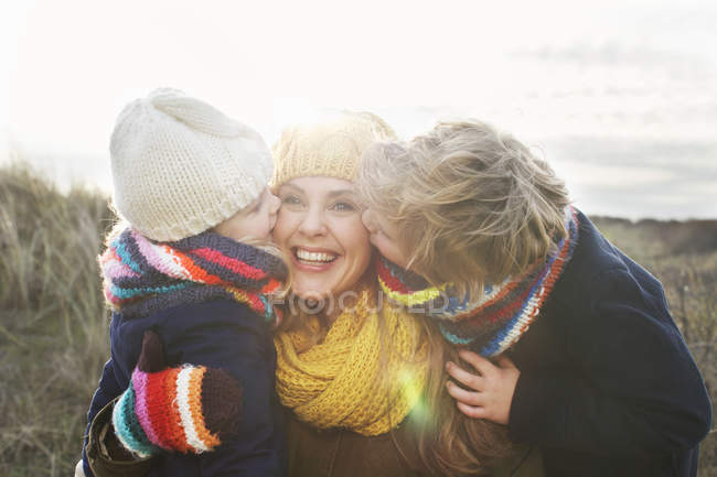 Mulher adulta média com filho e filha beijando sua bochecha na costa — Fotografia de Stock
