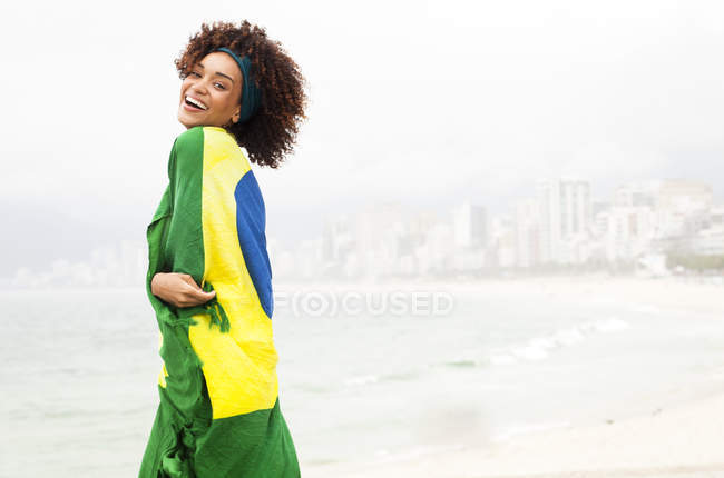 Portrait de jeune femme enveloppée dans le drapeau brésilien sur la plage d'Ipanema, Rio De Janeiro, Brésil — Photo de stock