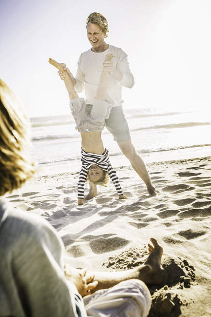 Father helping son with handstand on beach — Stock Photo