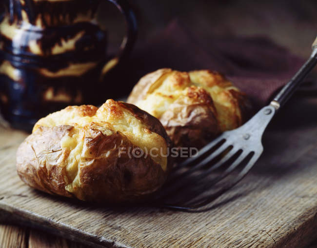Home-made jacket potatoes with cheddar cheese on rustic wooden board — Stock Photo