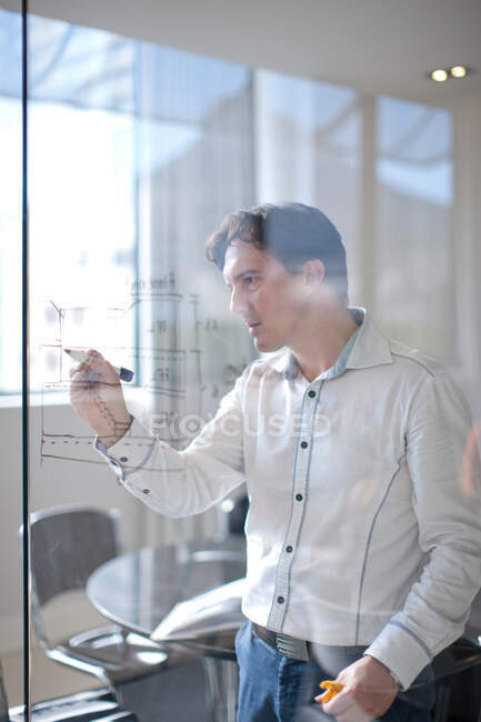 Homem desenhando planos arquitetônicos na parede de vidro — Fotografia de Stock