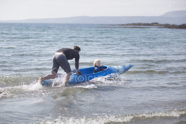 Padre empujando hijo en el agua en canoa - foto de stock